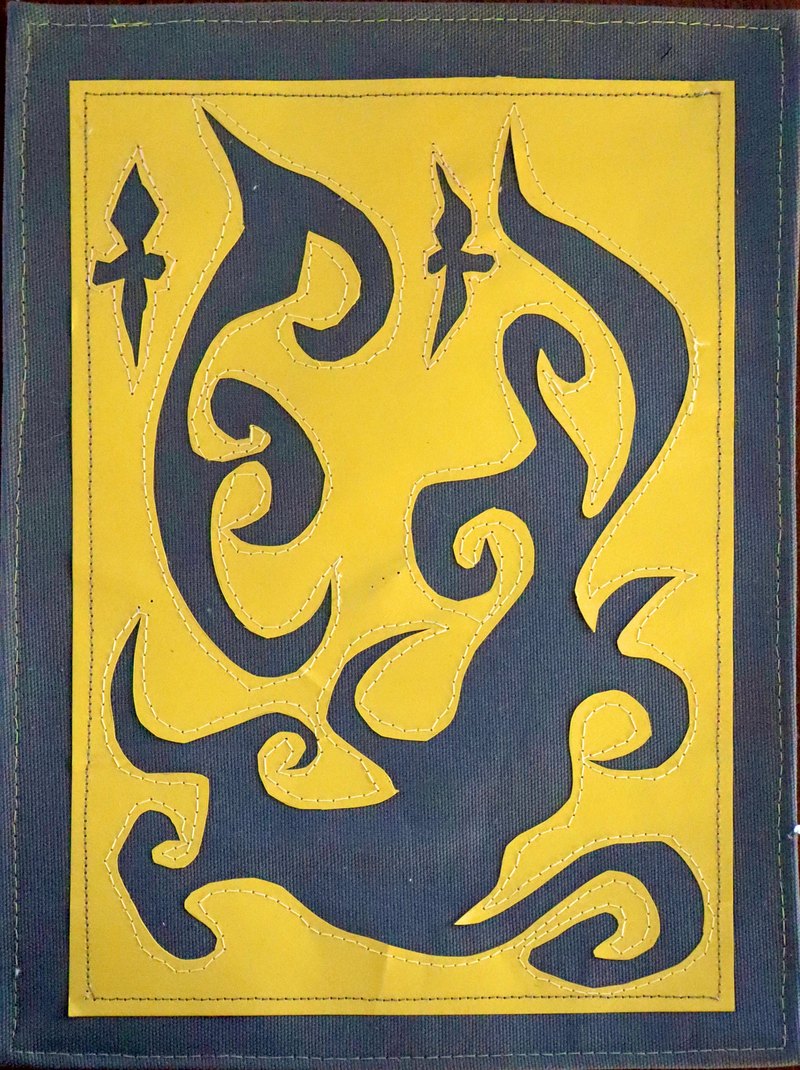 Yellow paper with dark navy cut-out shapes, sewn onto greyish canvas